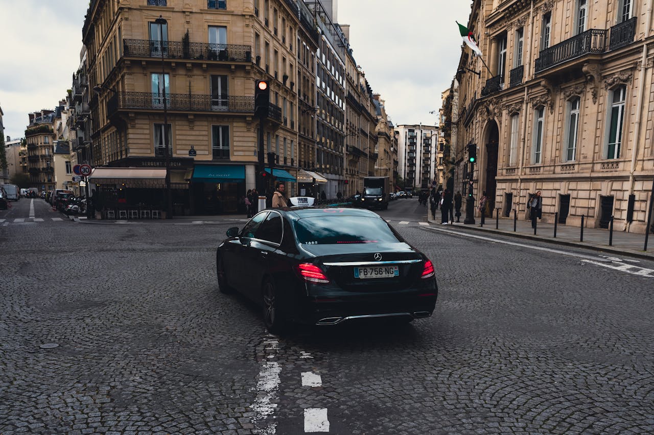 about-us Elegant black Mercedes-Benz taxi driving through charming Paris streets, highlighting urban sophistication.